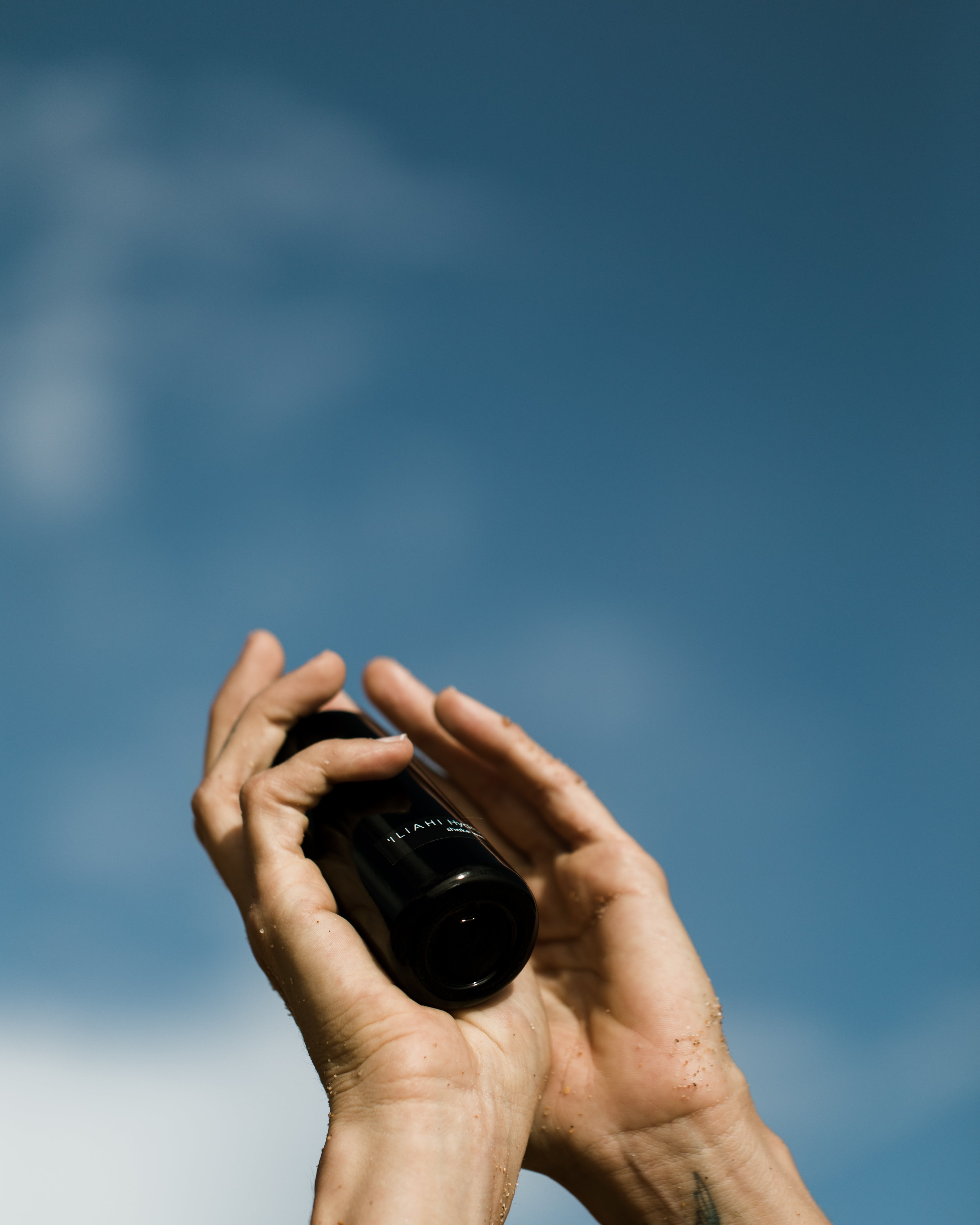 Hands holding an OSHAN glass bottle up against a blue sky