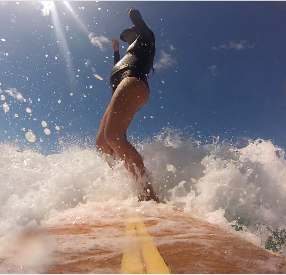A surfer rides a breaking wave, seen from the nose of the board
