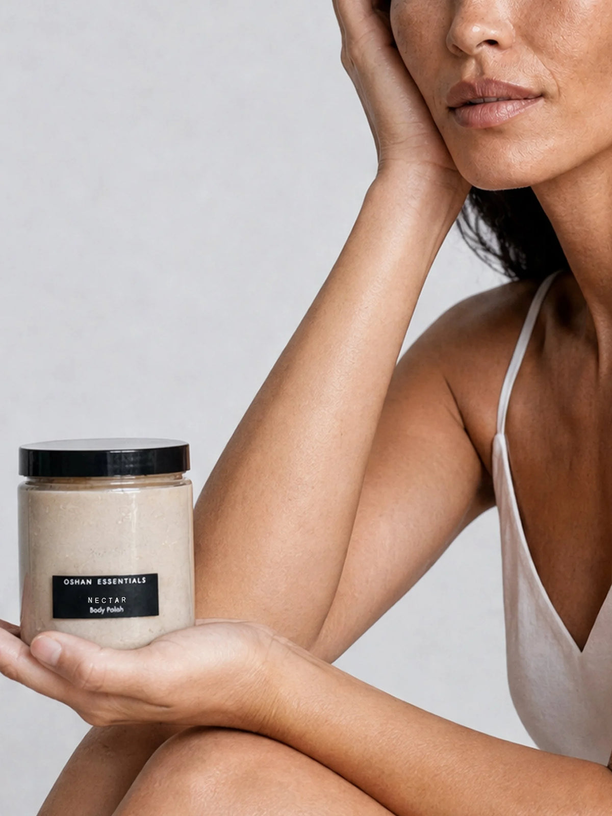 A woman holds a jar of NECTAR Body Polish in her palm