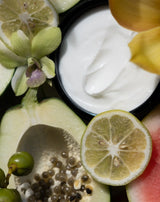 An open jar of NECTAR Crème Soufflé with cut lime and orchids