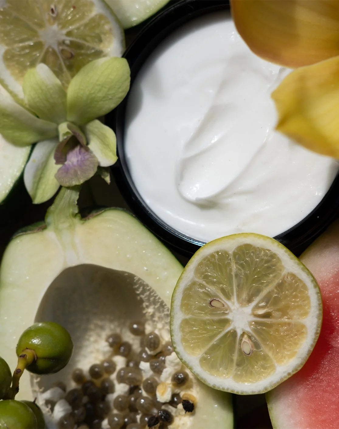 An open jar of NECTAR Crème Soufflé with cut lime and orchids