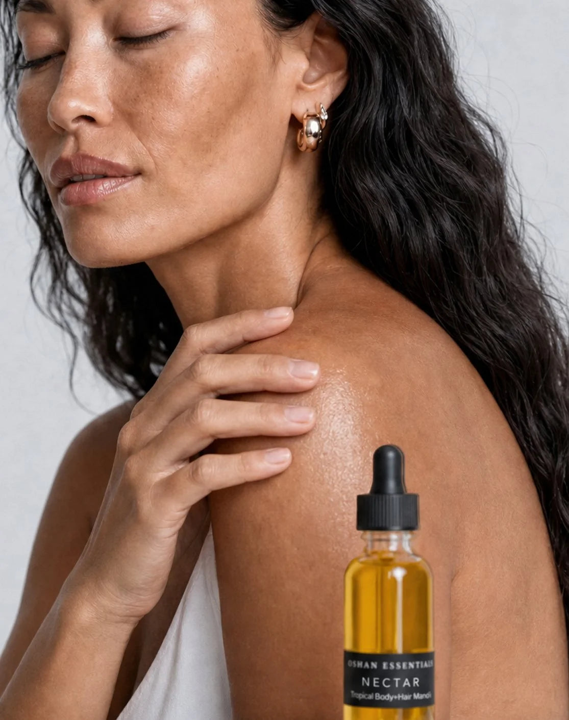 A woman touches her shoulder beside a bottle of NECTAR Manoʻi