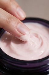 Close view of a fingertip swirling the pink OSHAN ʻĀLANA Radiance Face Soufflé in its jar.