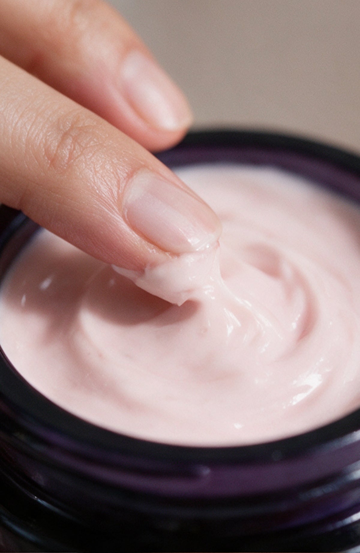 Close view of a fingertip swirling the pink OSHAN ʻĀLANA Radiance Face Soufflé in its jar.
