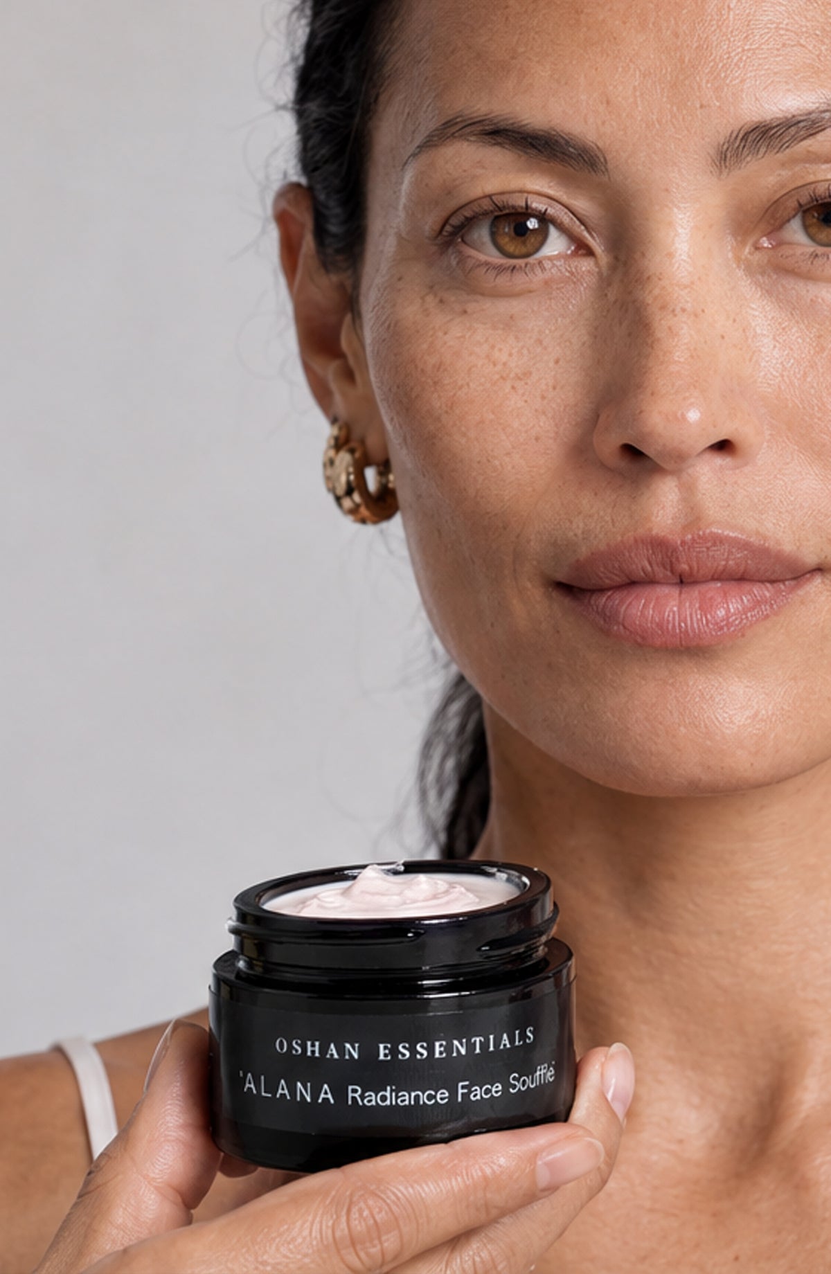 Model holding an open jar of OSHAN ʻĀLANA Radiance Face Soufflé at her chest.
