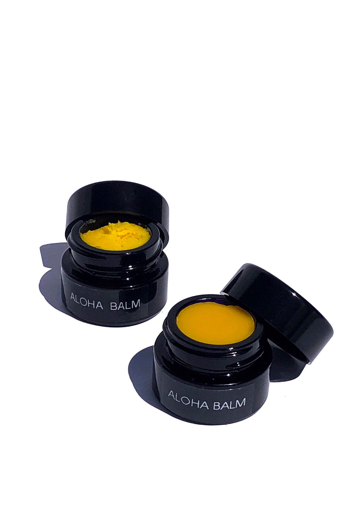 Open jars of OSHAN ALOHA Lip Vitality Balm and Whip showing the golden yellow color.