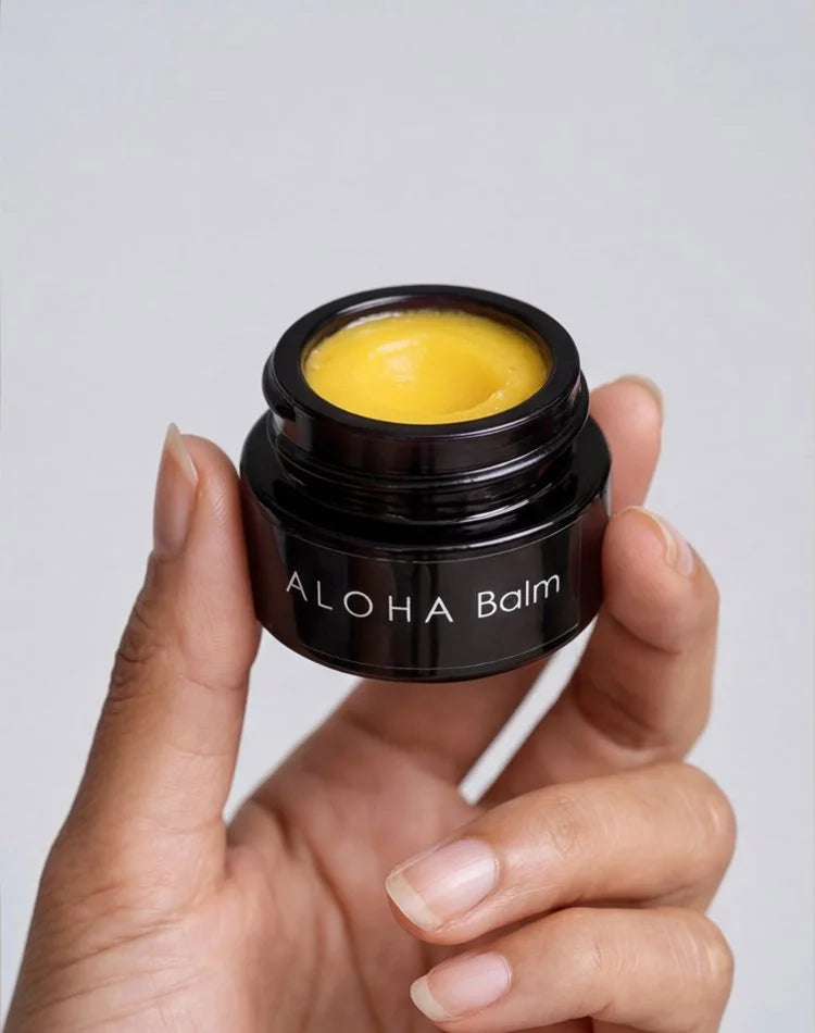 Hand holding an open jar of OSHAN ALOHA Lip Vitality Balm.