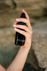 Hand holding the OSHAN ʻAWAPUHI Balancing Toner bottle against coastal rock.