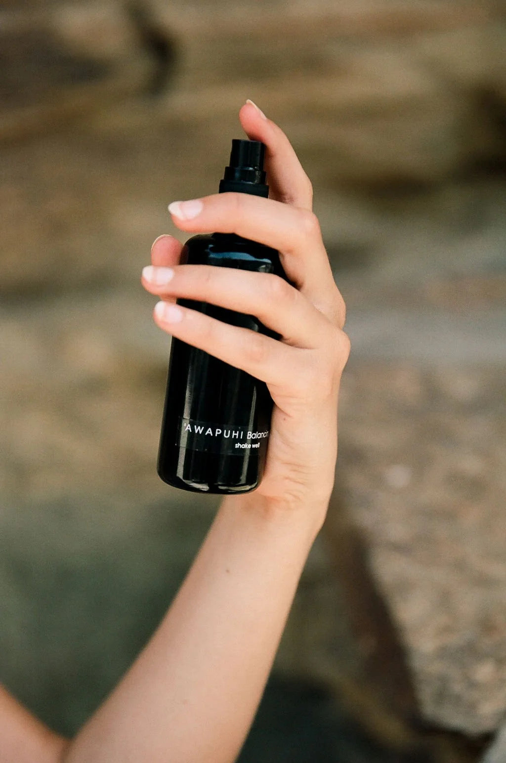 Hand holding the OSHAN ʻAWAPUHI Balancing Toner bottle against coastal rock.