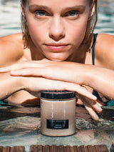 Model resting at the pool edge with a jar of OSHAN CALM ʻĀKALA Body Polish.