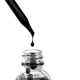 Black OSHAN ʻELE Clarifying Face Wash pouring into a clear glass bottle.