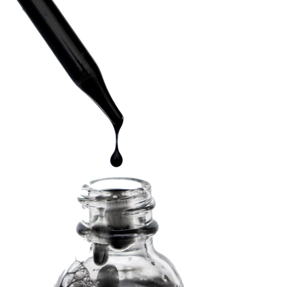 Black OSHAN ʻELE Clarifying Face Wash pouring into a clear glass bottle.