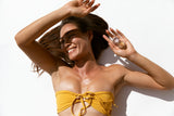 Model in a yellow swimsuit holding a jar of OSHAN HULALI Bronzing Face Luminizer.