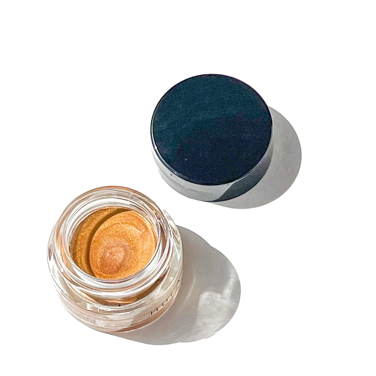 Open jar of OSHAN HULALI Bronzing Face Luminizer with its lid beside it.
