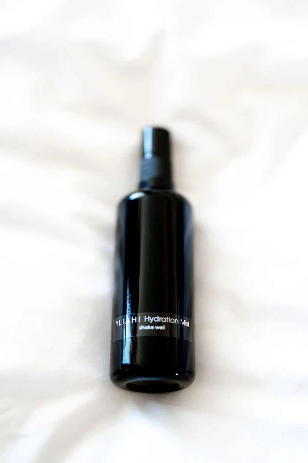 OSHAN ʻĪLIAHI Hydration Mist bottle resting on rumpled white linen.