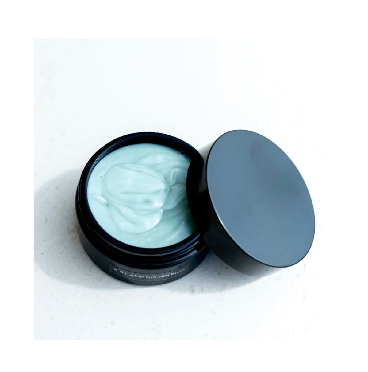 Open jar of OSHAN KAI After Sun Bliss Balm with the lid resting beside it.