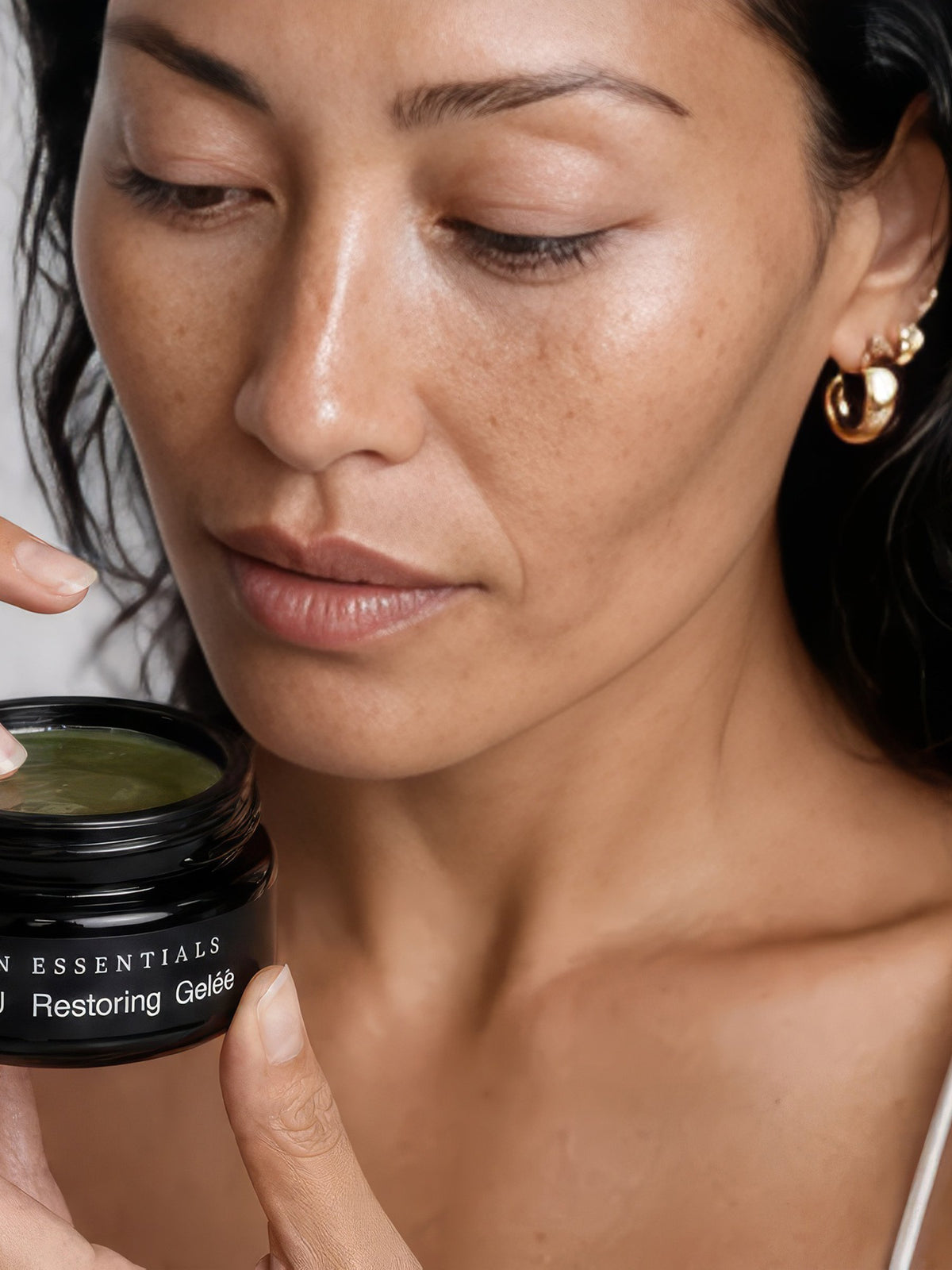 Model holding an open jar of OSHAN LĪHAU Restoring Gelée at her collarbone.
