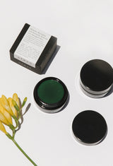 Open jar of OSHAN LĪHAU Restoring Gelée with its box and a yellow freesia stem.