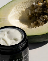 Open jar of OSHAN MĀLIE Cellular Hydration Mask beside a halved papaya.