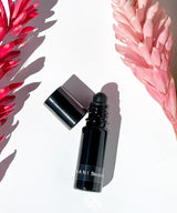 OSHAN NANI Beautifying Manoʻi roller bottle beside pink and red ginger flowers.