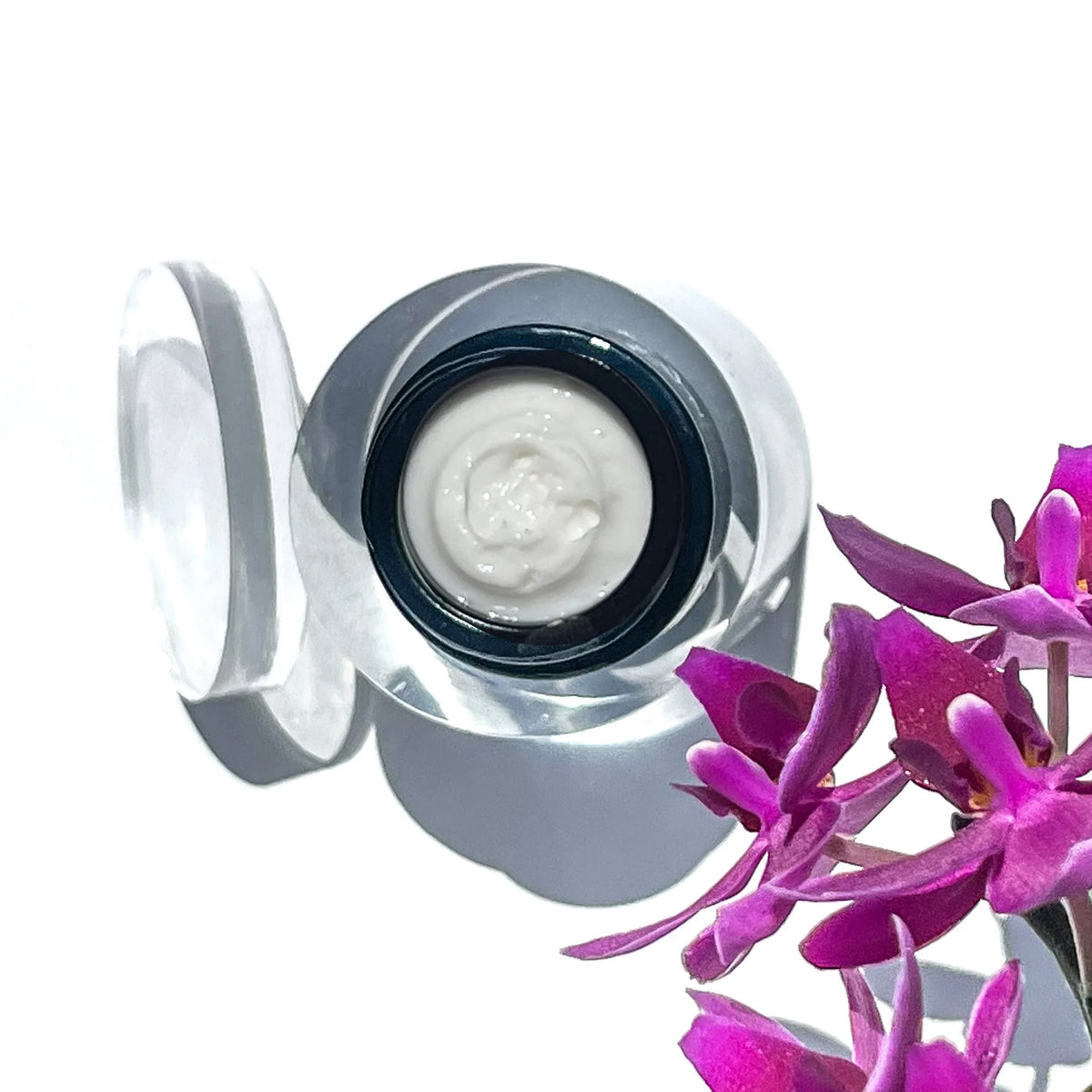 Open jar of OSHAN NOE Firming Eye Cream beside purple orchids.