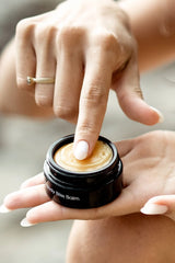 Finger taking OSHAN ʻŌLENA Body Bliss Balm from the open jar.