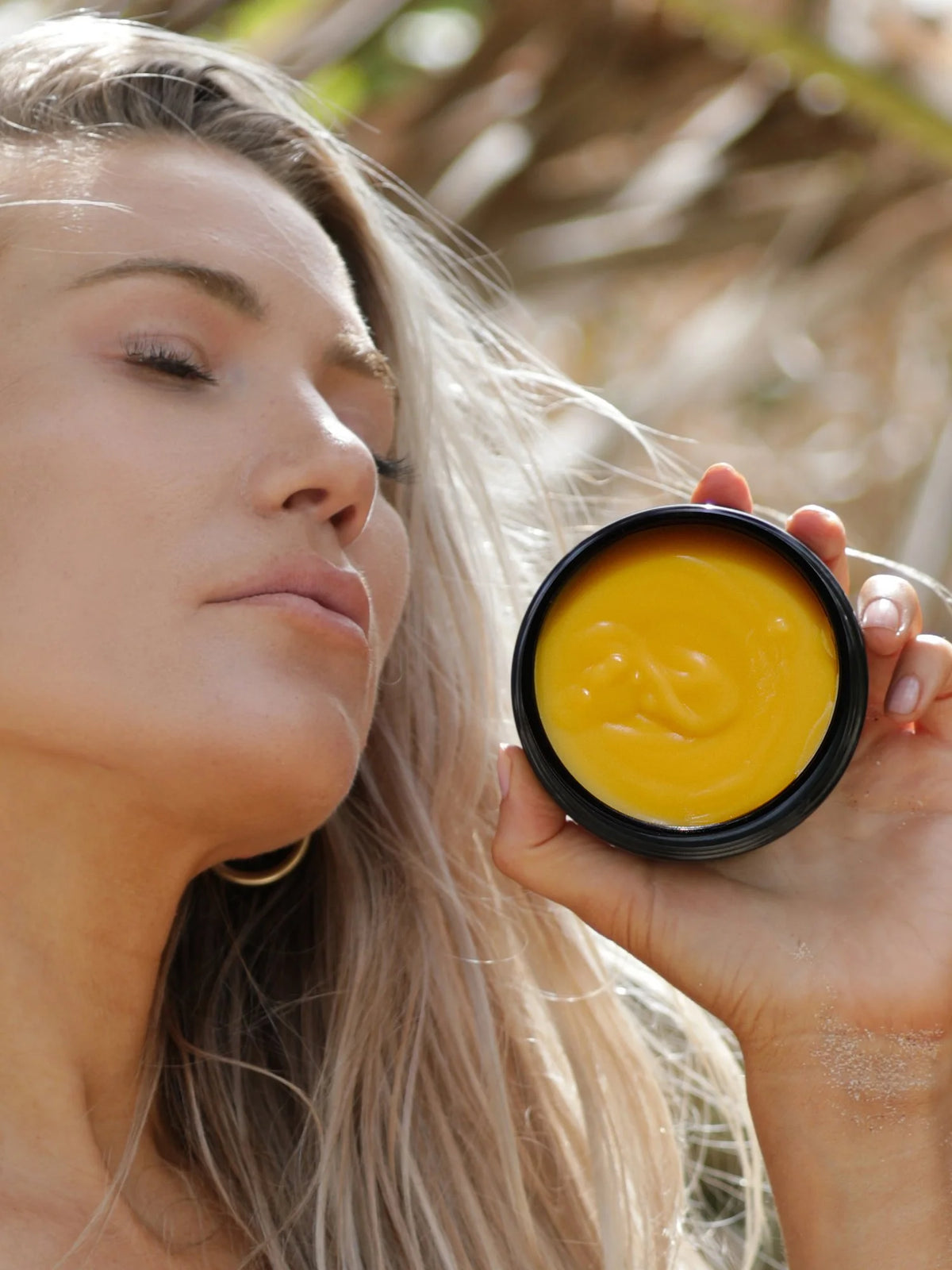 Model holding an open jar of OSHAN ʻŌLENA Body Bliss Balm beside her face.