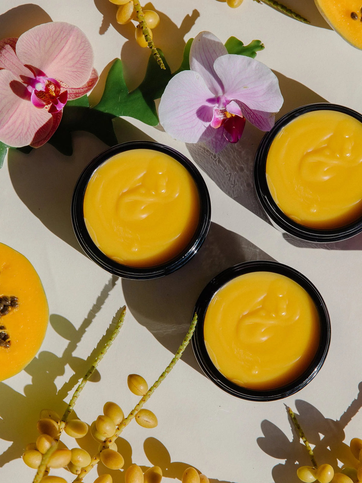 Three open jars of OSHAN ʻŌLENA Body Bliss Balm arranged with orchids.