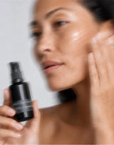 Model pressing OSHAN PALUPALU Hydration Serum into her cheek, bottle in hand.