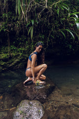 Model crouching in a jungle stream, the setting for the OSHAN SPA Set ritual.