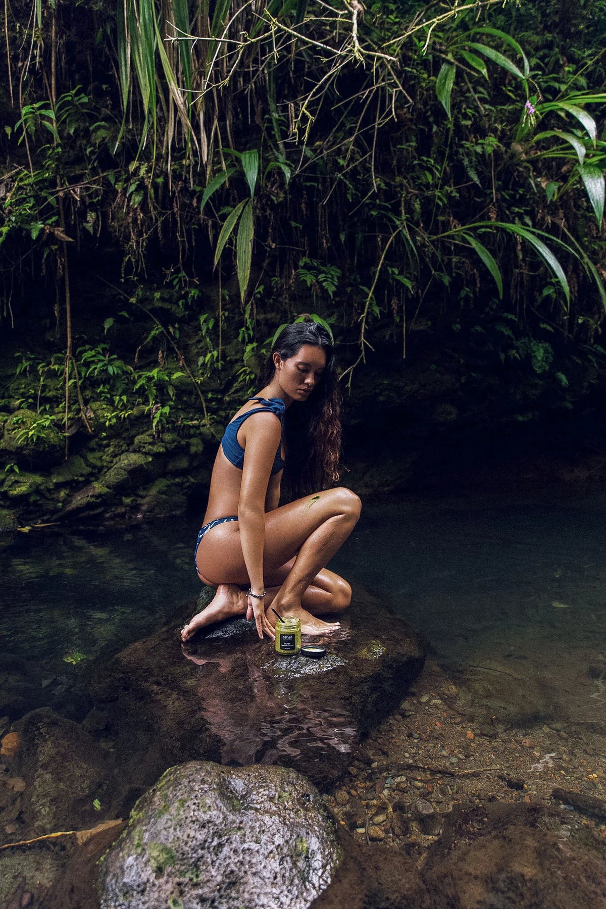 Model crouching in a jungle stream, the setting for the OSHAN SPA Set ritual.