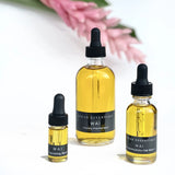 Three sizes of OSHAN WAI Invigorating Hair and Body Manoʻi beside a pink ginger flower.