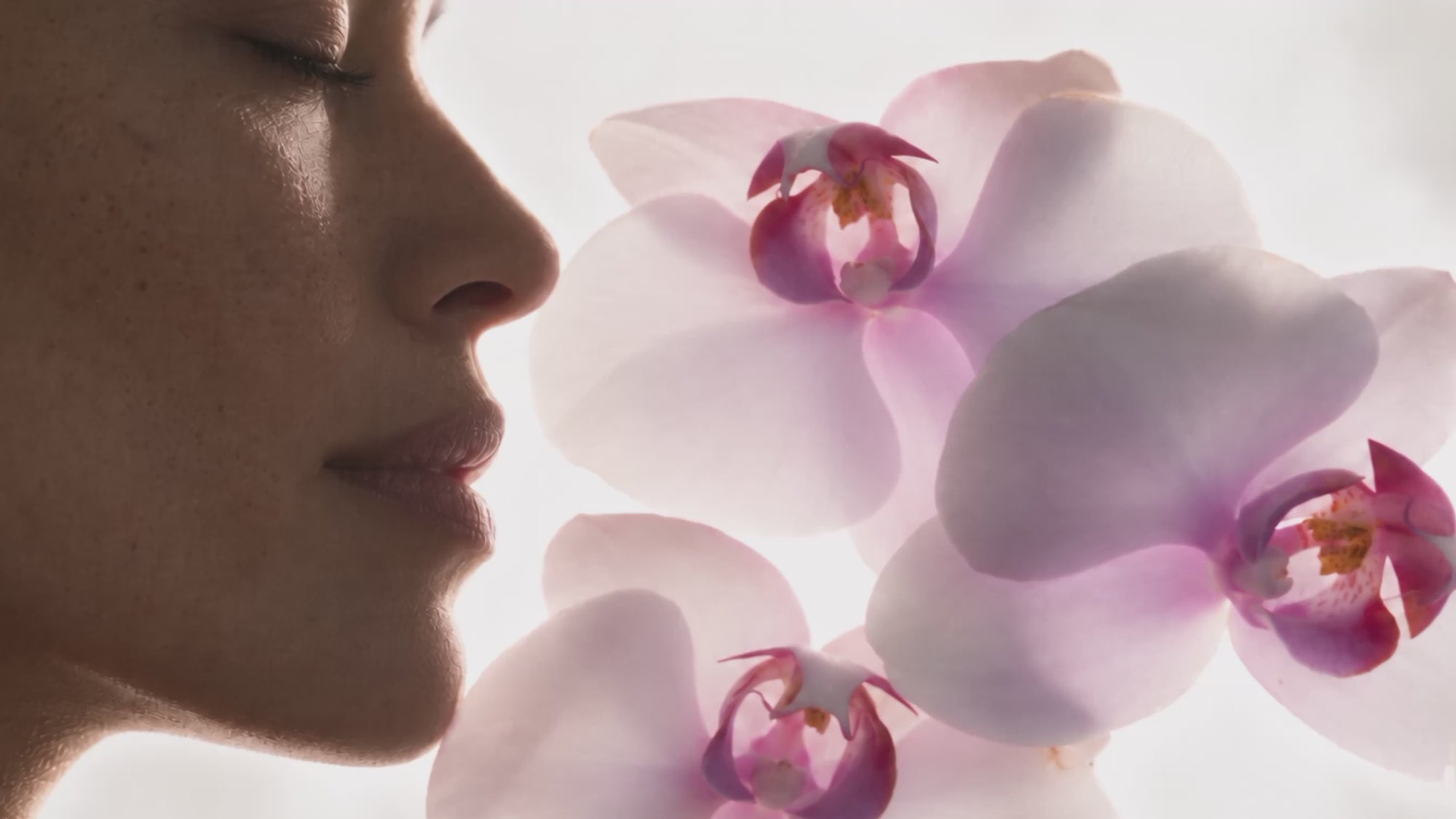 A woman with her eyes closed beside pale pink orchids