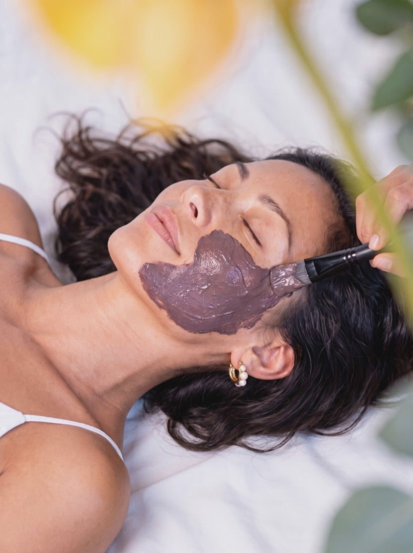 A woman lies back during a facial as a clay mask is brushed onto her face